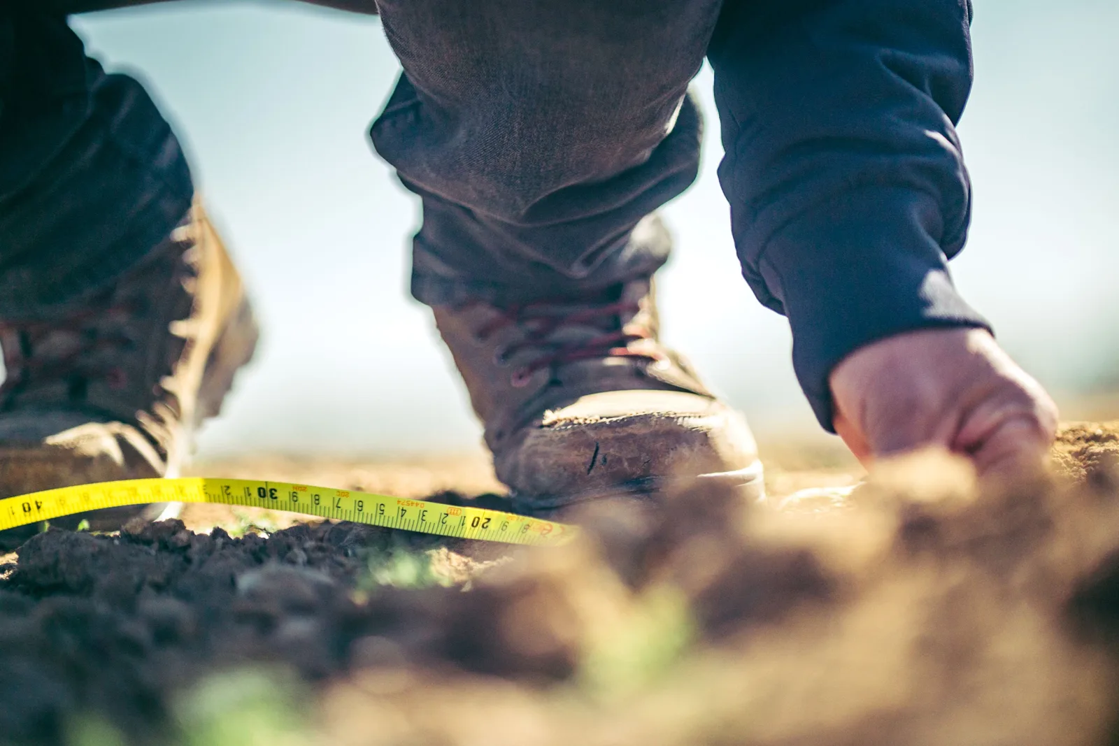 Une personne mesure au mètre ruban la terre d’un coin de jardin avant de l’aménager.